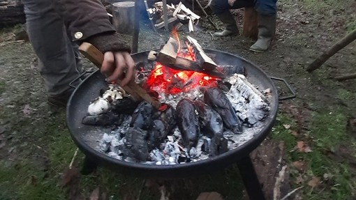 A man and two women build a fire in a metal bowl using twigs.