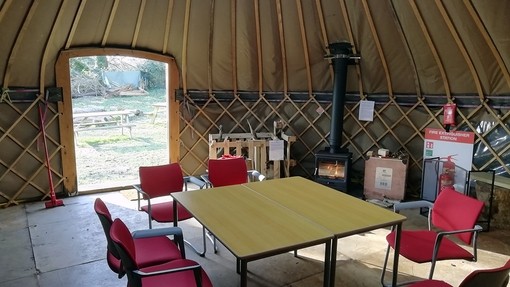 The yurt interior with a table and six chairs as well as a log burning stove to one side. 