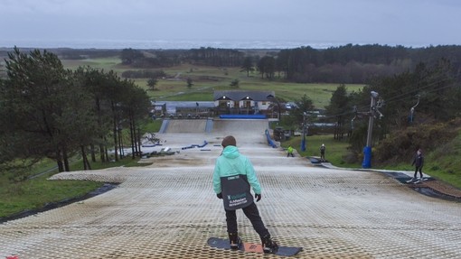 Student at the top of a dry ski slope on a snowboard