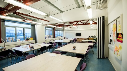 A large classroom brightly lit by overhead lights and with windows across one wall..