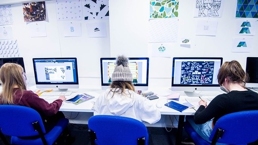 Three students creating designs on Apple Mac computers.
