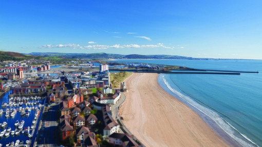 Llun o Abertawe yn cynnwys y traeth a’r harbwr o’r awyr