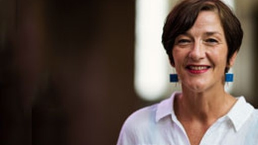 Wearing a white shirt and big boxy blue earrings, Karen MacKinnon smiles towards the camera. 