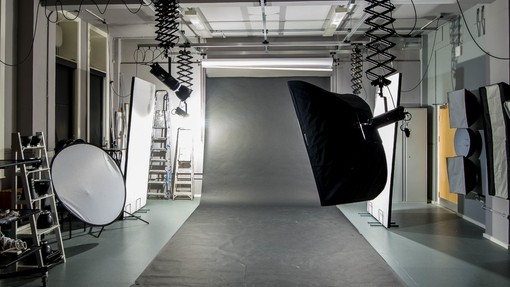 A photography studio with movable overhead lights, screens, and a long roll of black fabric spread across the floor..
