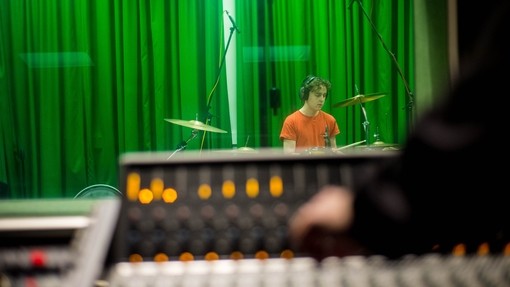 Student mixing music while another person plays the drums