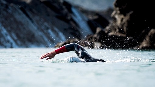 A rocky bay with a man swimming through the water in a wetsuit.