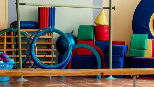 Colourful plastic hoops, baskets of balls for sport, and various kinds of foam mattresses piled along the wall of a school gym.