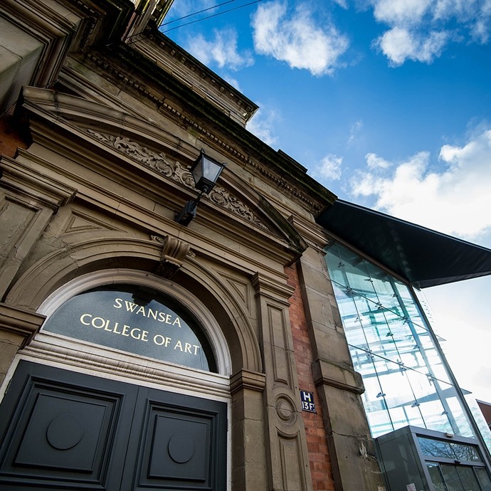 A Victorian doorway with Swansea College of Art written in gold in the transom window; in the background the modern glass extension. 